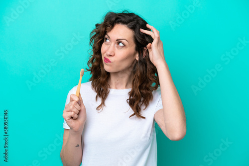Young caucasian woman brushing teeth isolated on blue background having doubts and with confuse face expression