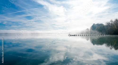 Jetty at the lake in the fog. Misty landscape in the morning. Idyllic nature by the water. Rest and relaxation. 