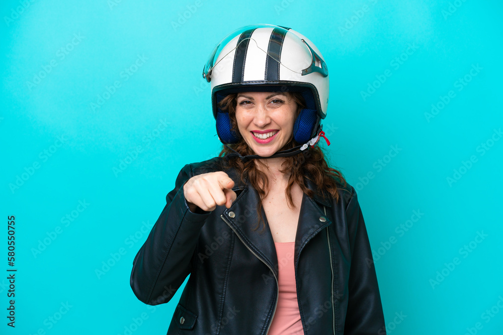 Young caucasian woman with a motorcycle helmet isolated on blue background pointing front with happy expression