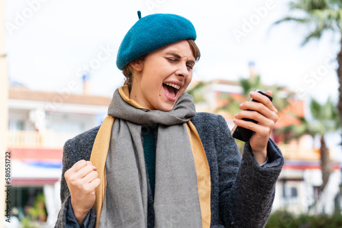 Brunette woman at outdoors using mobile phone and doing victory gesture © luismolinero
