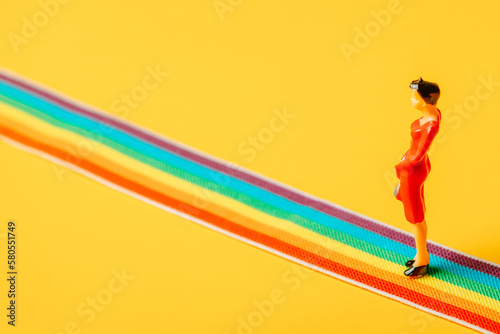 Adult woman figure stand on rainbow LGBT strip on yellow background