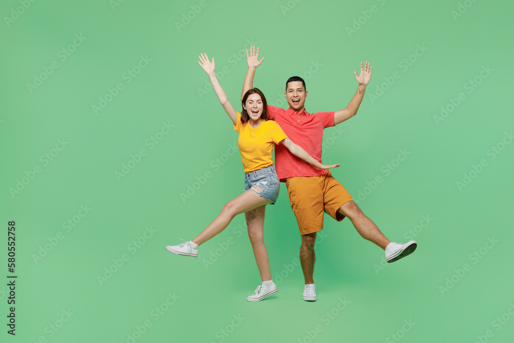 Full body overjoyed cool fun happy young couple two friends family man woman wears basic t-shirts together look camera raise up hands isolated on pastel plain light green background studio portrait. Full body overjoyed cool fun happy young couple two friends family man woman wears basic t-shirts together look camera raise up hands isolated on pastel plain light green background studio portrait.