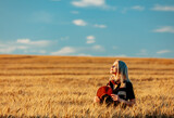 Blonde woman in black dress and hat with scarf in wheat field in autumn season time