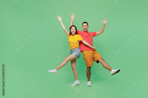Full body overjoyed cool fun happy young couple two friends family man woman wears basic t-shirts together look camera raise up hands isolated on pastel plain light green background studio portrait.