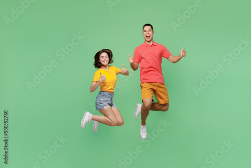 Full body satisfied happy fun cool young couple two friends family man woman wear basic t-shirts together showing thumb up like gesture isolated on pastel plain light green background studio portrait.