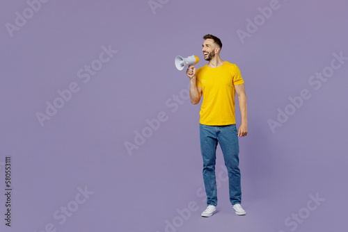 Full body young surprised shocked excited fun man wear yellow t-shirt hold in hand megaphone scream announce discounts sale Hurry up isolated on plain pastel light purple background Lifestyle concept