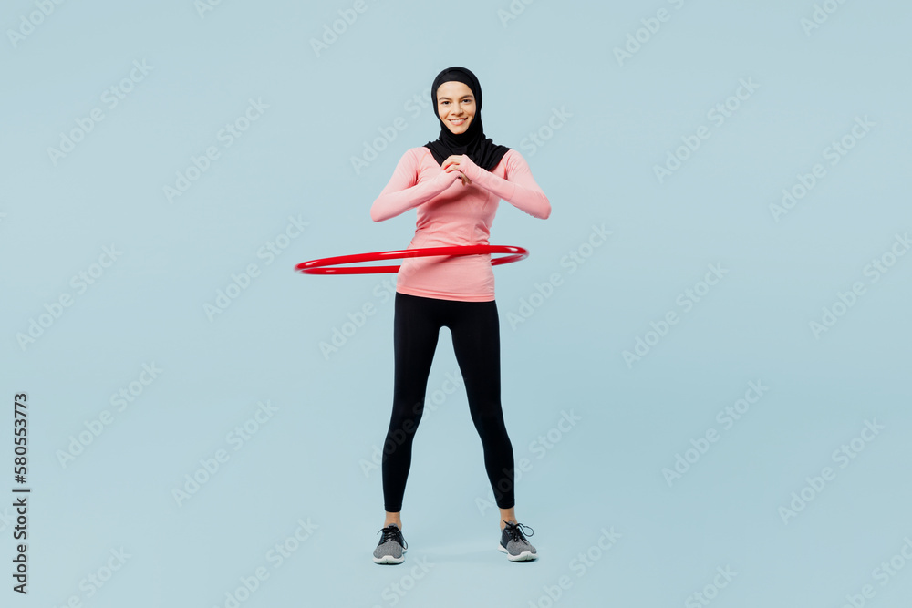 Full body young asian muslim fitness trainer sporty woman wear pink abaya hijab spend time in home gym use hula hoop look camera isolated on plain blue background studio Workout sport fit abs concept. Full body young asian muslim fitness trainer sporty woman wear pink abaya hijab spend time in home gym use hula hoop look camera isolated on plain blue background studio Workout sport fit abs concept.