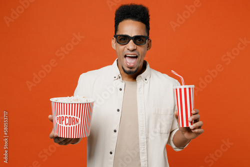 Canvastavla Young cheerful excited fun man of African American ethnicity in 3d glasses watch movie film holding bucket of popcorn cup of soda pop in cinema isolated on plain orange red background studio portrait