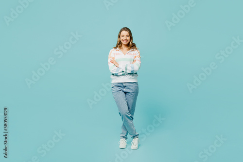 Full body smiling happy fun cheerful young woman wearing striped hoody look camera holding hands crossed folded isolated on plain pastel light blue cyan background studio portrait. Lifestyle concept.