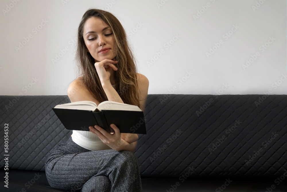 Young woman on couch reading and holding a book, reading, notions of home and comfort, copy space for text. Young woman on couch reading and holding a book, reading, notions of home and comfort, copy space for text.
