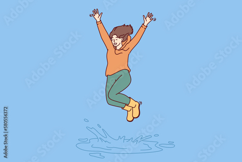 Happy woman jumping in puddle enjoying first autumn rain after hot summer. Girl in good mood in casual clothes jumps standing in puddle, receiving positive emotions from long-awaited walk 