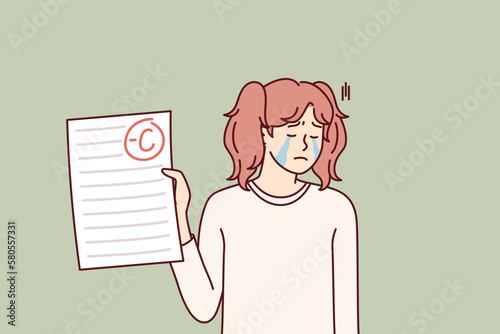 Crying teenage girl depressed because of negative mark on test or exam paper. Unhappy schoolgirl is sad after receiving bad grade from teacher for extracurricular work and needs help of tutor 