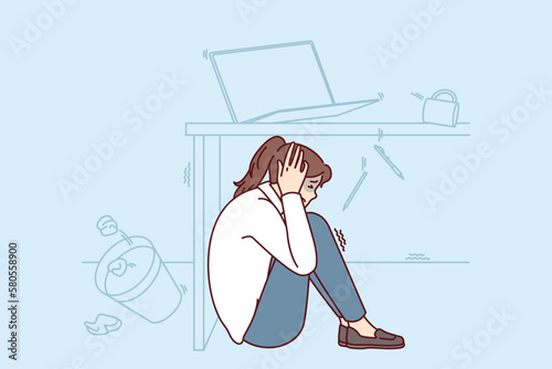 Frightened woman wait out earthquake hiding under office desk to save herself during building collapse. Girl sits on floor fleeing earthquake or tornado and other natural anomalies