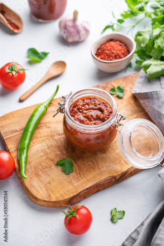 Homemade tomato sauce for pizza or pasta in a jar on a wooden board on a light background with fresh vegetables and herbs.