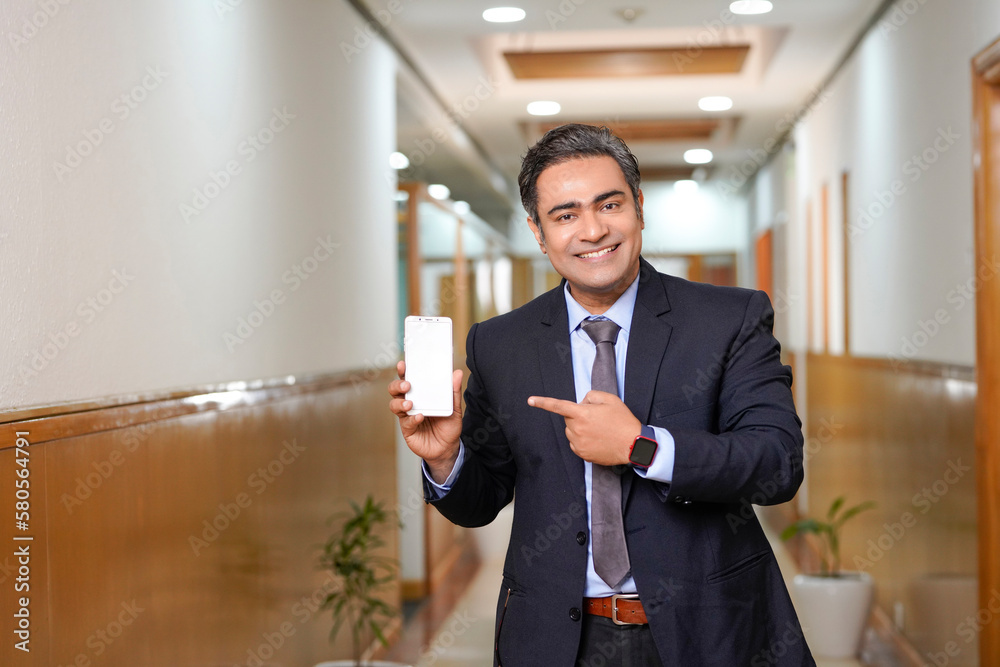 Fototapeta premium Young businessman showing smartphone screen on office background.