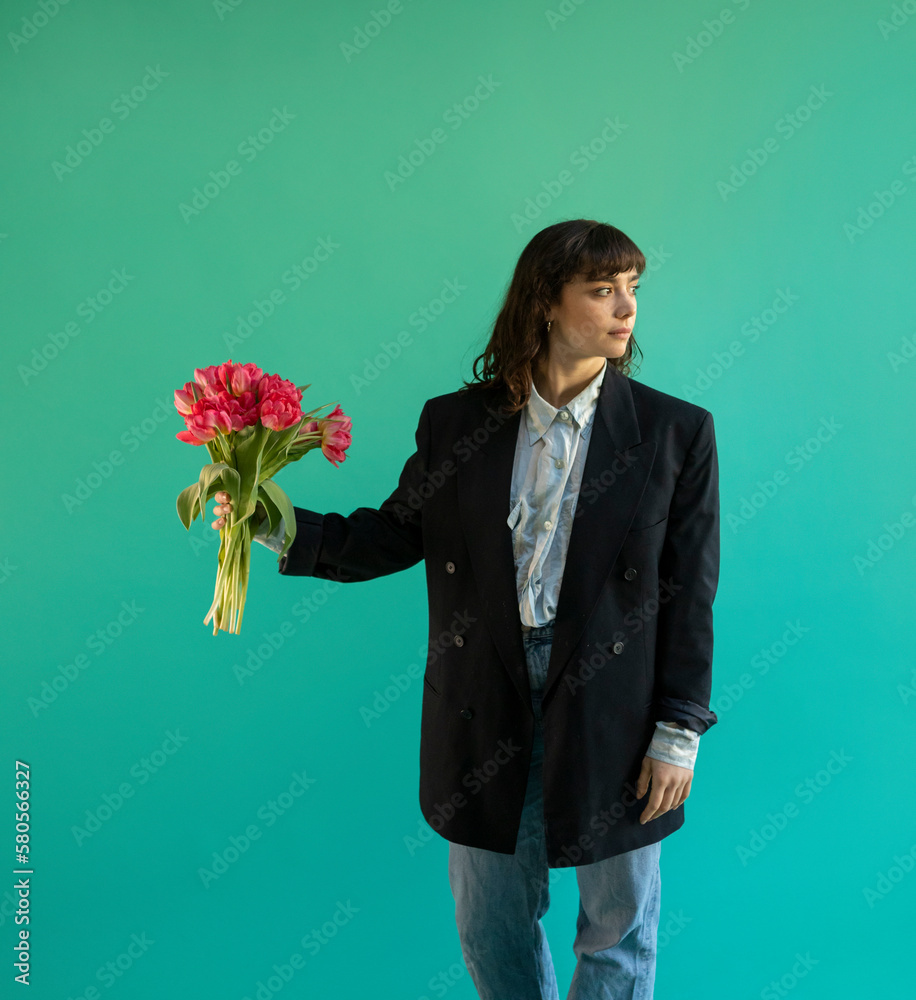 Woman wearing blazer holding bunch of pink tulips against green background