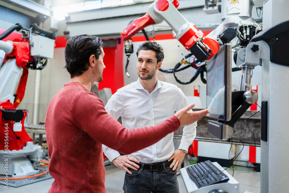 Engineer explaining robotic arm to colleague at industry Engineer explaining robotic arm to colleague at industry