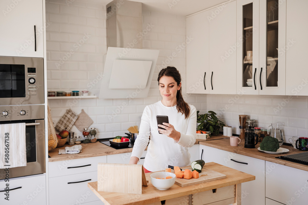 Smiling woman using mobile phone in kitchen at home Smiling woman using mobile phone in kitchen at home