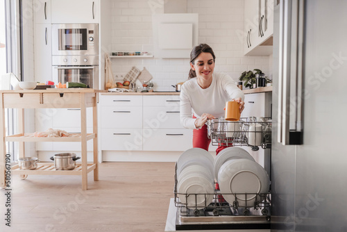 Woman arranging crockery in dishwasher at home photo