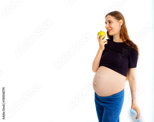 Pregnant woman propose apple for her belly copy space. Beautiful expectant lady having fresh snack  gray studio background. Healthy nutrition and pregnancy concept  copy space