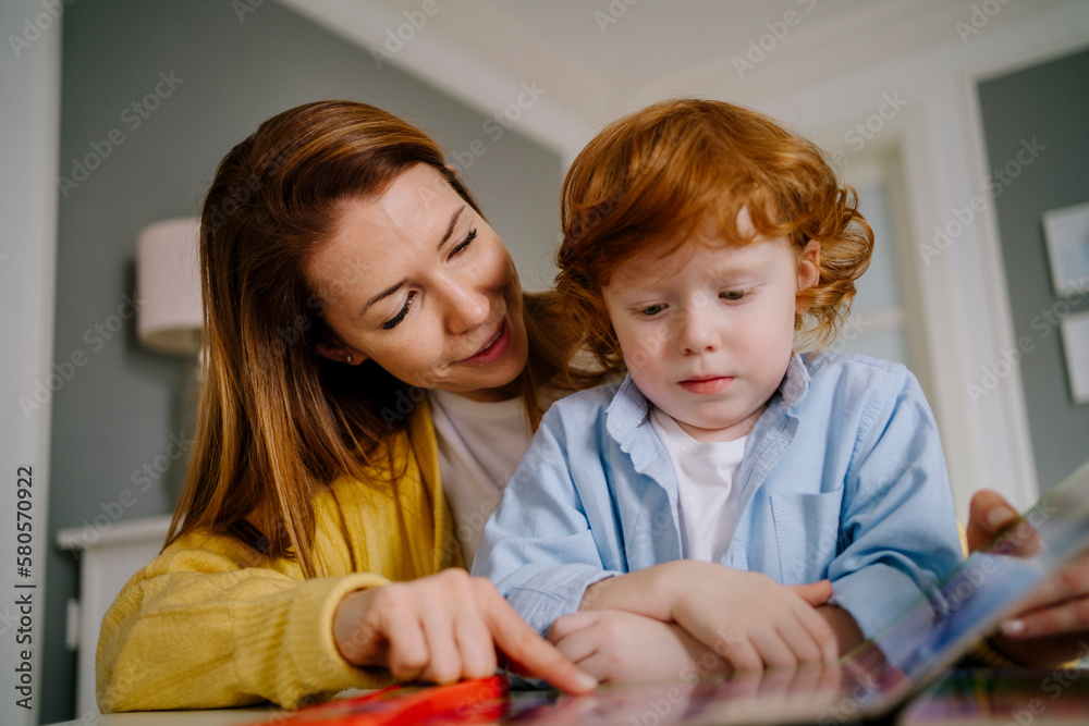Mother assisting son reading book at home Mother assisting son reading book at home