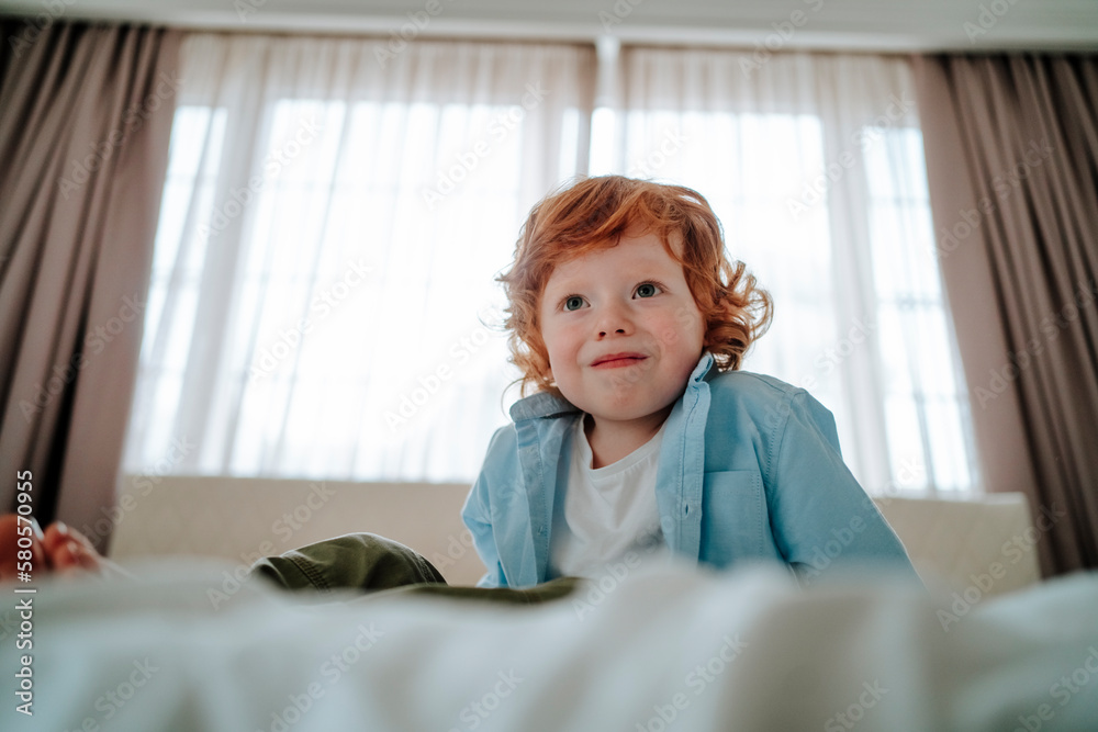 Redhead boy sitting on bed at home Redhead boy sitting on bed at home