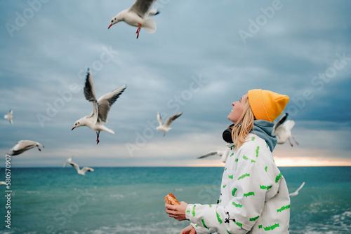 Happy young woman feeding seagulls hovering at shore photo