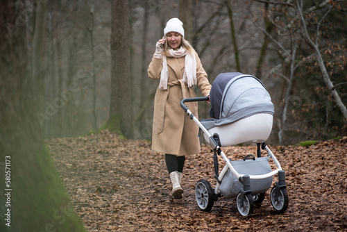 Woman with baby stroller talking on smart phone in forest photo