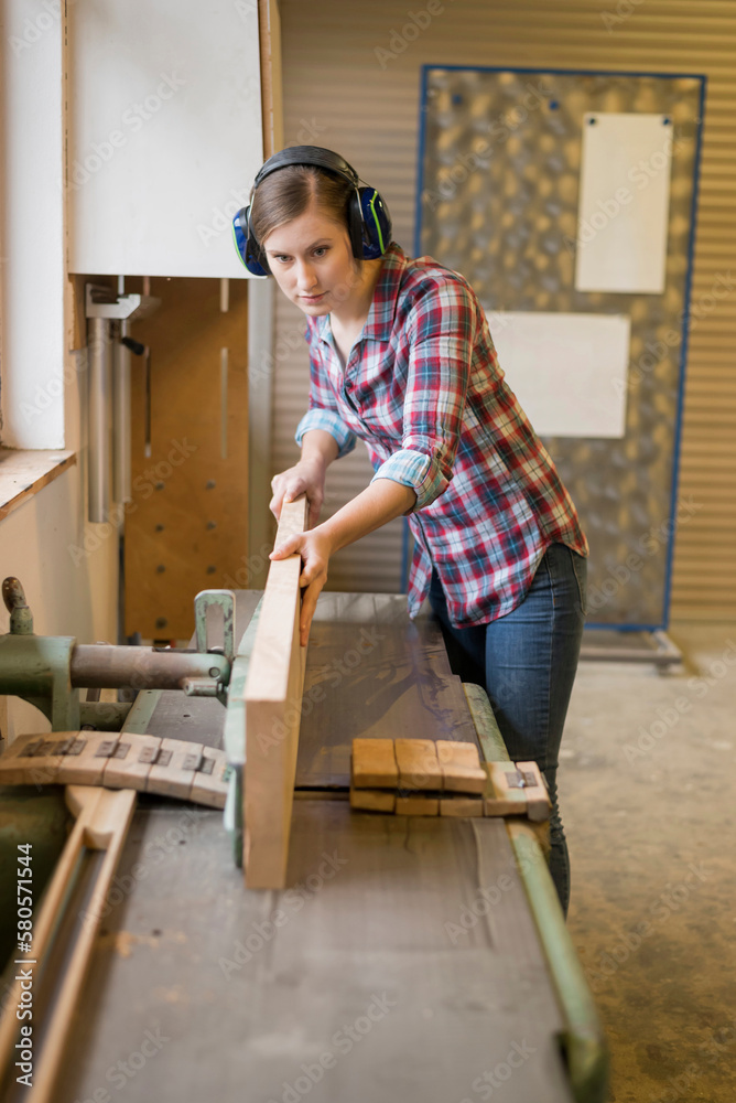 Craftswoman wearing ear protectors cutting wood in workshop Craftswoman wearing ear protectors cutting wood in workshop