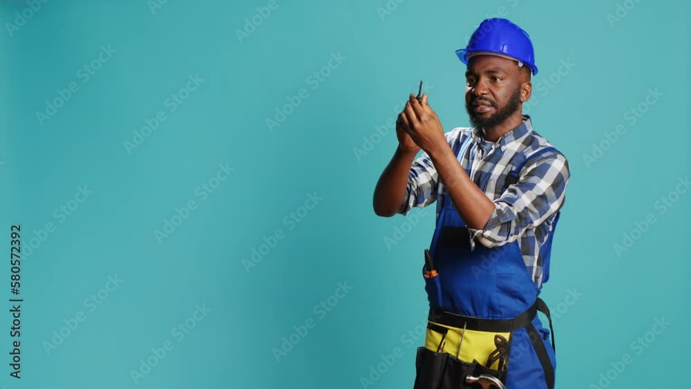Carpenter in overalls holding screwdriver in studio, using handy instrument to screw nails. Construction engineer working with manual utility tool, screwing something over blue background.