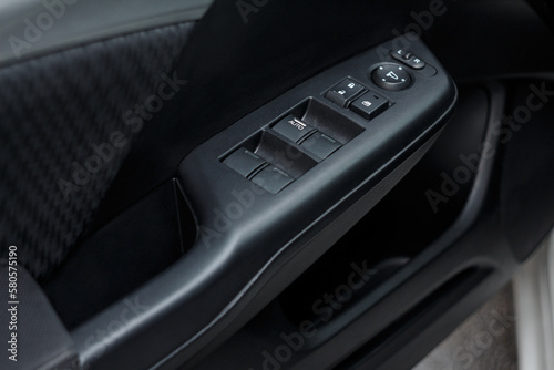 Arm rest with door lock buttons, window and mirror control panels. Close-up of a modern car door details, from inside view. Driver's seat