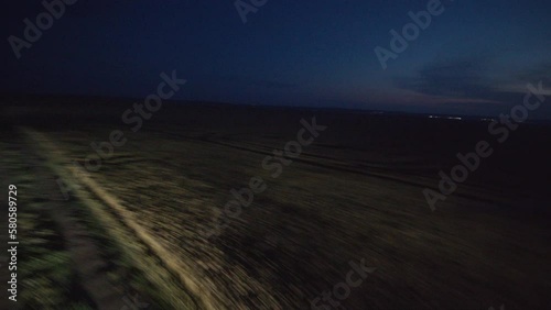 Footage from drone of fast car with highlights driving by straight ground road near field in village at night. Countryside view. Outdoors