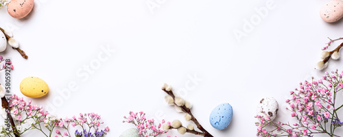 Beautiful Easter composition with spring flowers and colorful quail eggs over white background. Springtime and Easter holiday banner concept with copy space. Top view