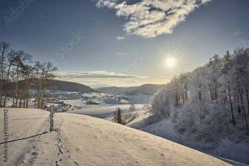 Winterlandschaft im aargauischen Fricktal. Sonnenaufgang über dem Wald mit Blick auf das Dorf Möhntal.