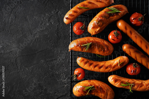 Grill and barbecue sausage on board, with tomatoes and rosemary on black background