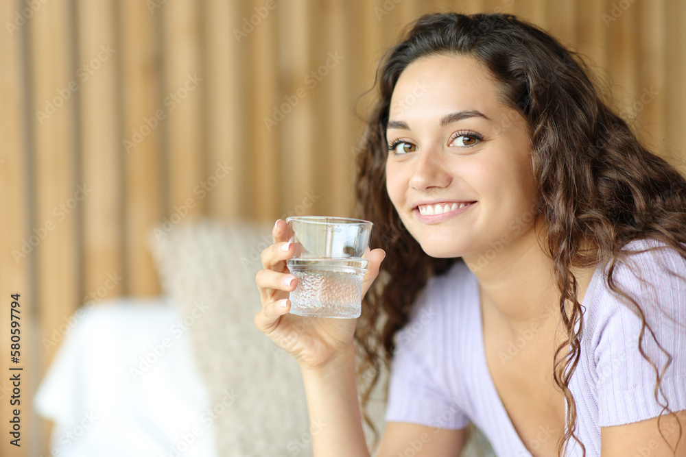 Happy woman holding water glass looks at you Happy woman holding water glass looks at you