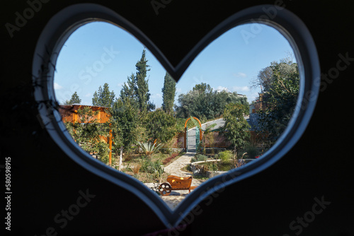Traditional rural hospitality, looking through a heart shaped window on a landscape with a village garden
