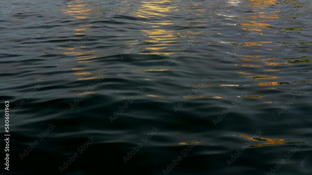 Orange and yellow lights reflect smooth rippling dark green water. Mid shot Orange and yellow lights reflect smooth rippling dark green water. Mid shot