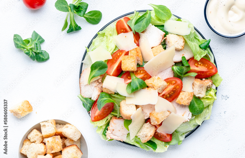Caesar salad with chicken, iceberg salad, croutons, parmesan cheese and tomatoes with caesar dressing. White table background, top view Caesar salad with chicken, iceberg salad, croutons, parmesan cheese and tomatoes with caesar dressing. White table background, top view