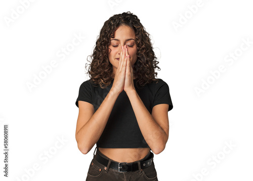 Bild auf Leinwand Radiant young woman with stunning curls holding hands in pray near mouth, feels confident