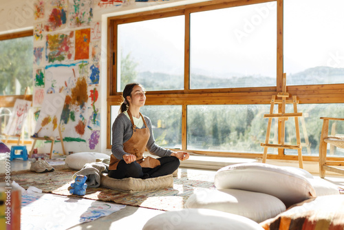 Young woman artist sitting on floor doing yoga exercise at art studio.Mindful activity and art therapy concept photo