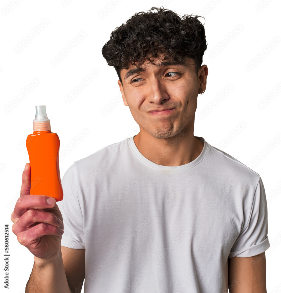 A young latin man holding a solar protection cream confused, feels doubtful and unsure. A young latin man holding a solar protection cream confused, feels doubtful and unsure.