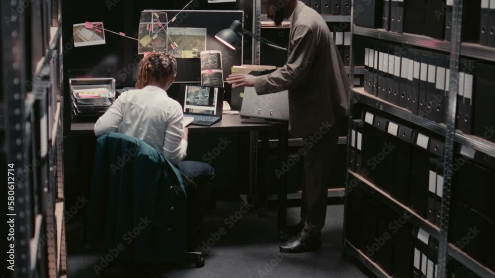 Team of inspectors analyzing case reports for details in police archive, using criminal records to catch suspect. Law enforcement officers reading evidence files, looking at surveillance footage. Team of inspectors analyzing case reports for details in police archive, using criminal records to catch suspect. Law enforcement officers reading evidence files, looking at surveillance footage.