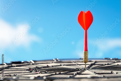 Dart in bullseye of dartboard target with blue sky background hitting target, goal and success