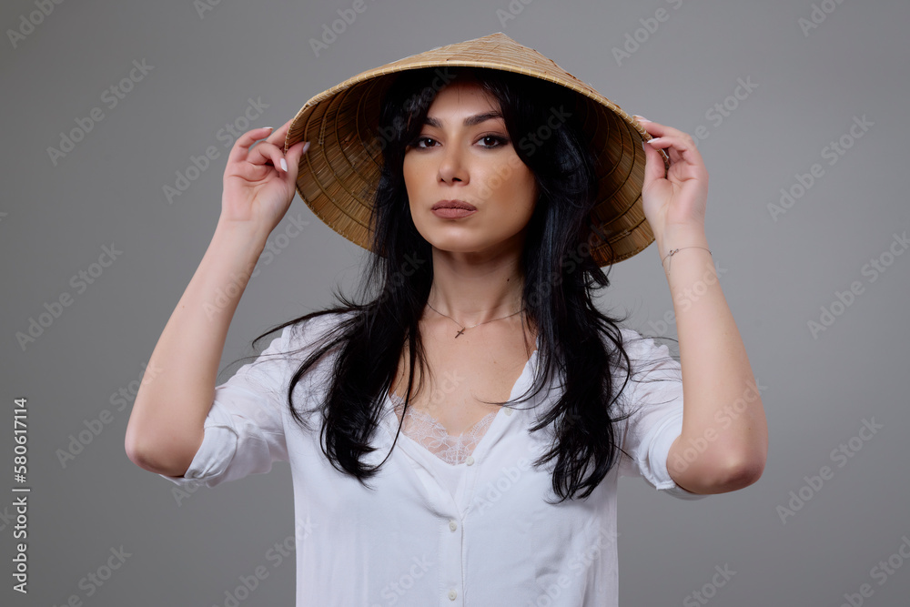 a beautiful brunette woman with a Vietnamese hat posing in the studio. a beautiful brunette woman with a Vietnamese hat posing in the studio.