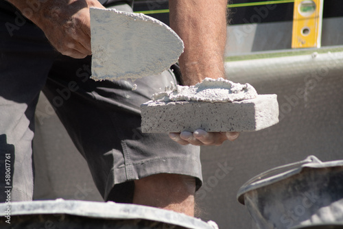 close up of the hands of a bricklayer applying cement mortar to a brick