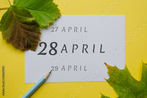 28 april day of month on a white sheet and the dates of the day earlier and later, written in simple pencil. Decoration with green leaves and yellow background.