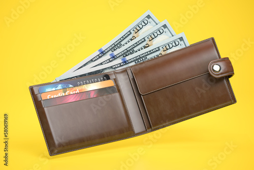 Open leather wallet with dollars and credit cards on yellow background.