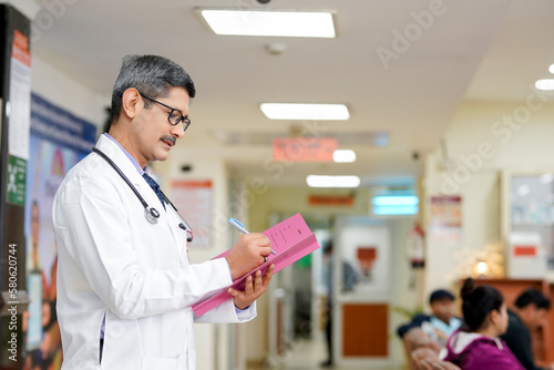 Indian male doctor writing medical record in file his patient.