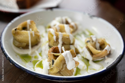 Smoked eggplant rolls on top of mozzarella cheese slices, in yogurt sauce, olive oil and pesto